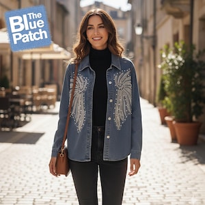 May include: A light blue denim jacket with pearl and rhinestone embellishments in a wing-like design. The jacket has a button-down front and is worn over a black turtleneck and black jeans. The text "The Blue Patch" is in the upper left corner.