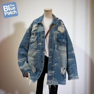 May include: A distressed blue denim jacket with a light wash and ripped details. The jacket has a classic collar, button-down front, and multiple pockets. The Blue Patch logo is in the upper left corner.