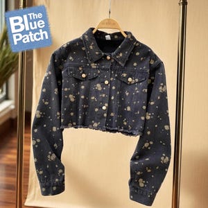 May include: A cropped denim jacket in dark blue with a splattered beige pattern. The jacket has a classic collar, button-up front, and frayed hem. The Blue Patch logo is visible in the upper left corner.