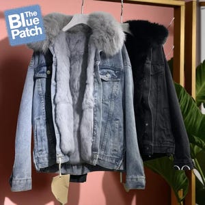 Peut inclure: Deux vestes en jean avec garniture en fourrure sont suspendues. L'une est bleu clair avec de la fourrure grise, l'autre est noire avec de la fourrure noire. Les vestes ont des fermetures à boutons et un design en jean classique. Le logo Blue Patch est visible.