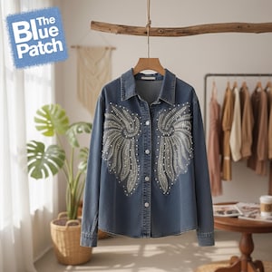 May include: A mid-wash denim shirt featuring a wing design made of pearl-like beads. The shirt has a standard collar, button-down closure, and long sleeves. The blue patch logo is in the upper left corner.