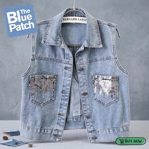 May include: Light blue denim vest with silver sequin pocket accents. The vest has a collared neckline and button-up front. The text "The Blue Patch" is visible in the upper left corner. The vest is hanging on a hanger.