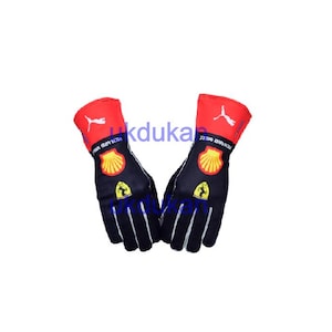 Peut inclure: Une paire de gants de course noirs et rouges. Les gants ont un poignet rouge avec un logo Puma blanc et une paume noire avec un logo Shell jaune et un logo Ferrari. Conçus pour le sport automobile.