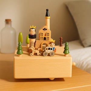 May include: A wooden music box with a castle design, including a tower, arched doorway, and figures of a king and a prince. The box features a horse-drawn carriage and trees. The colour scheme is natural wood tones with green and black accents.