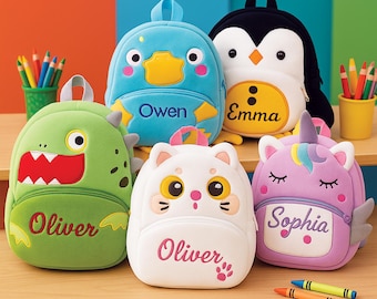 May include: A collection of colorful, character-shaped backpacks. Designs include a green dinosaur, a blue duck, a white cat, a black and white penguin, and a purple unicorn. Each backpack has a name embroidered on it.