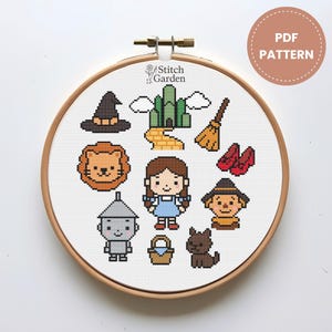 Pode incluir: Um padrão de ponto cruz com personagens e elementos de O Mágico de Oz, incluindo Dorothy, o Homem de Lata e o chapéu da Bruxa Má. O design é exibido em um bastidor de bordado de madeira, com o texto "PDF PATTERN".