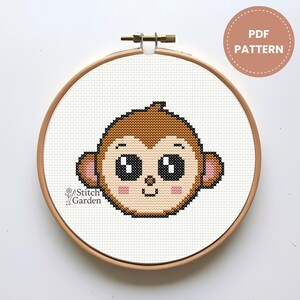 Pode incluir: Padrão de ponto cruz de um rosto de macaco de desenho animado com olhos grandes, pelo marrom e bochechas rosadas, em um bastidor de bordado de madeira. O texto "PDF PATTERN" está em um círculo. O texto "Stitch Garden" está no canto inferior esquerdo.