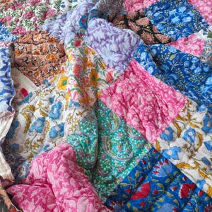 May include: A colourful patchwork quilt with floral and paisley designs in pink, blue, purple, and green. The quilt is made of quilted fabric and has a soft, textured appearance. The design is a mix of different fabric squares.
