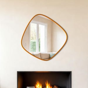Peut inclure: Un salon moderne avec un miroir géométrique à cadre doré au-dessus d'une cheminée. Une table basse ronde en bois repose sur un tapis blanc. Un fauteuil en osier et une grande plante en pot complètent le décor.