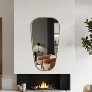 May include: A modern living room with a minimalist design. A large, gold-framed mirror hangs above a fireplace with a burning fire. The room features brown leather chairs, a gray sofa, and a black coffee table. A tall plant adds a touch of nature.