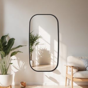 Peut inclure: Un grand miroir rectangulaire à cadre noir est accroché à un mur blanc. Le miroir reflète une pièce avec un canapé, des plantes et de la lumière naturelle. La pièce a une palette de couleurs neutres avec une esthétique minimaliste. Le miroir mesure environ 152 cm de haut.