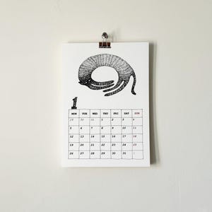May include: A white wall calendar page for the month of January featuring a black ink illustration of a curled cat at the top. Below the illustration is a grid with the number 1, days of the week, and dates from 29 to 31 and 1 to 31.