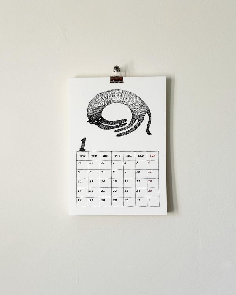 May include: A white wall calendar page for the month of January featuring a black ink illustration of a curled cat at the top. Below the illustration is a grid with the number 1, days of the week, and dates from 29 to 31 and 1 to 31.