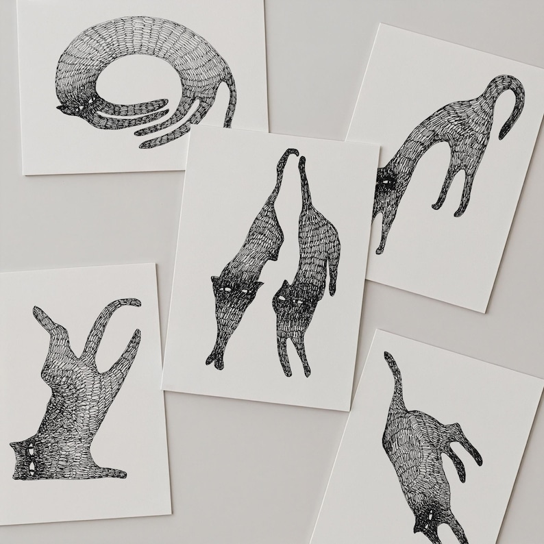 May include: A collection of five rectangular white greeting cards, each featuring a distinct black ink illustration of a cat. The cats are depicted in various elongated, contorted poses with detailed cross-hatched line work throughout their bodies.