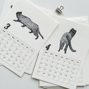 May include: A stack of white paper calendar pages featuring black ink illustrations of cats. One page shows the number 3 with a cat in motion, and another shows the number 4 with a standing cat. Each page includes a grid of days and dates.
