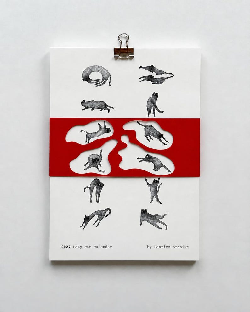 May include: A 2027 wall calendar titled 2027 Lazy cat calendar by Pantics Archive, featuring black and white illustrations of cats in various poses. A red paper band with irregular cutouts overlays the center of the white calendar page.