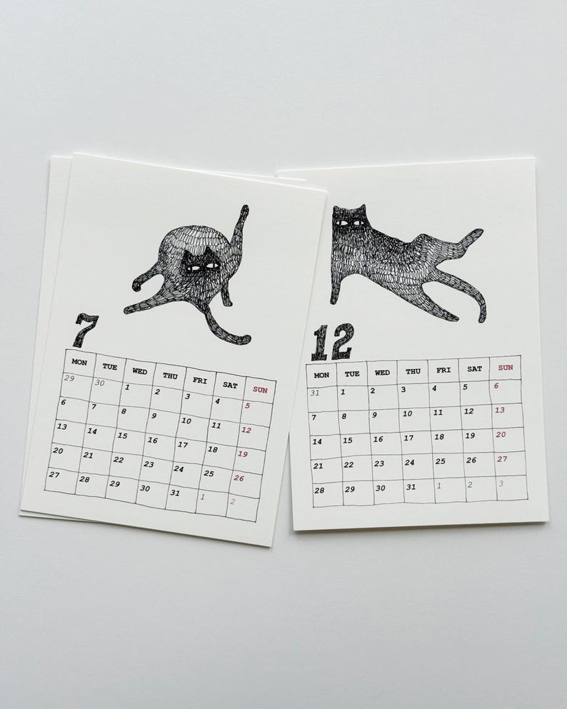 May include: Two white calendar pages featuring black ink illustrations of cats. The left page shows the number 7 with a cat grooming itself, while the right page shows the number 12 with a cat stretching. Each page includes a grid of days.