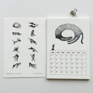 Könnte beinhalten: Ein zweiseitiger Kalender mit weißem Hintergrund. Die linke Seite zeigt schwarze Katzenillustrationen, während die rechte Seite ein Kalenderraster für Januar zeigt. Der Text "2026 Lazy cat calendar" ist sichtbar.