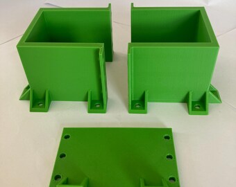 Puede incluir: Tres componentes verdes brillantes, impresos en 3D, de forma cuadrada. Dos son cajas con la parte superior abierta y pestañas de montaje. El tercero es una base plana con elementos de montaje. Todas las piezas tienen un acabado mate suave.
