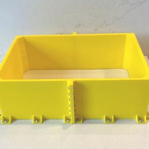 May include: A vibrant yellow rectangular container with a trapezoidal shape. The container has a flat base and is assembled with metal fasteners. The container is designed for storage or display.