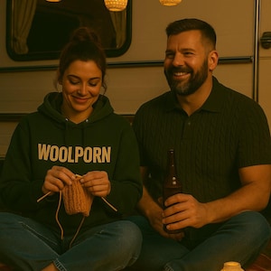Op de afbeelding: Een stel zit op een rood geruite deken, verlicht door lichtslingers en decoratieve lantaarns. Een persoon draagt een groene hoodie met "WOOLPORN" en breit met wol. De ander houdt een bierfles vast.