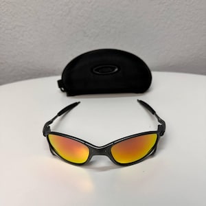 May include: Black sunglasses with orange and yellow lenses and a black case. The sunglasses have a sleek, modern design with a black frame and curved temples. The lenses have a gradient effect, transitioning from orange to yellow.