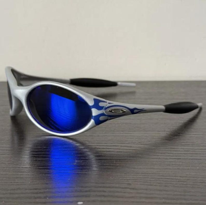 Puede incluir: Gafas de sol plateadas con lentes azules. Las patillas presentan un dise&ntilde;o de llamas azules. Las puntas de las patillas son negras. Estas gafas ofrecen protecci&oacute;n ocular y un aspecto elegante.