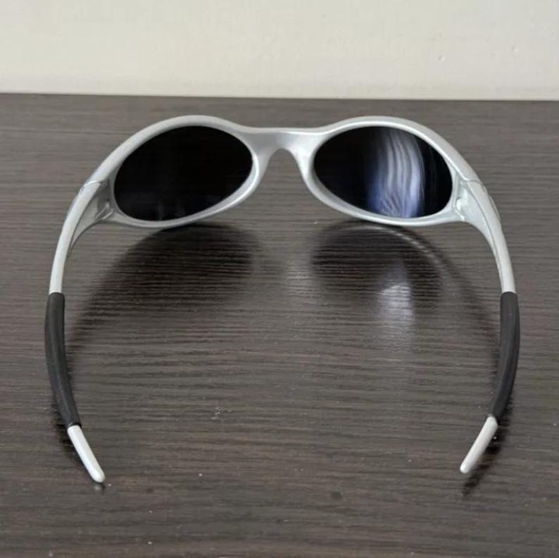 Puede incluir: Gafas de sol plateadas con lentes oscuras. Las gafas tienen un dise&ntilde;o moderno con patillas curvas y puntas de goma negra para mayor comodidad. Las lentes ovaladas ofrecen una cobertura completa.