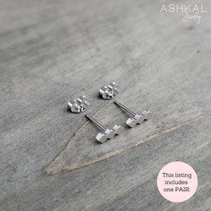 May include: A pair of silver earrings with a wavy design. The earrings are on a wooden surface. This listing includes one PAIR.