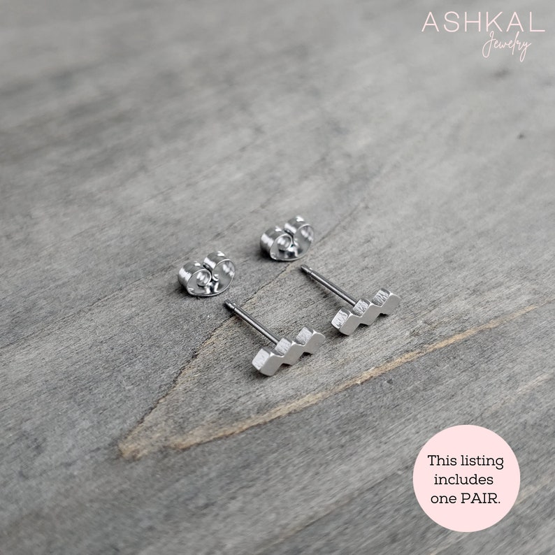 May include: A pair of silver earrings with a wavy design. The earrings are on a wooden surface. This listing includes one PAIR.