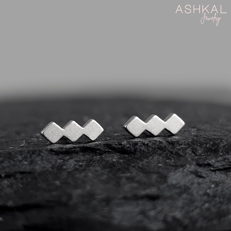 May include: A pair of silver geometric earrings with a zig-zag design. The earrings are small and delicate, and they are perfect for everyday wear.