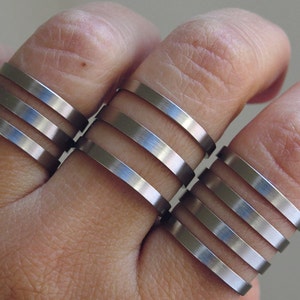 May include: A set of five silver rings stacked on a finger. The rings are all the same width and have a smooth, polished finish.