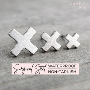 May include: Three silver cross-shaped stud earrings, the largest is in the foreground, the smallest is in the background.  Surgical Steel - Waterproof - Non-Tarnish
