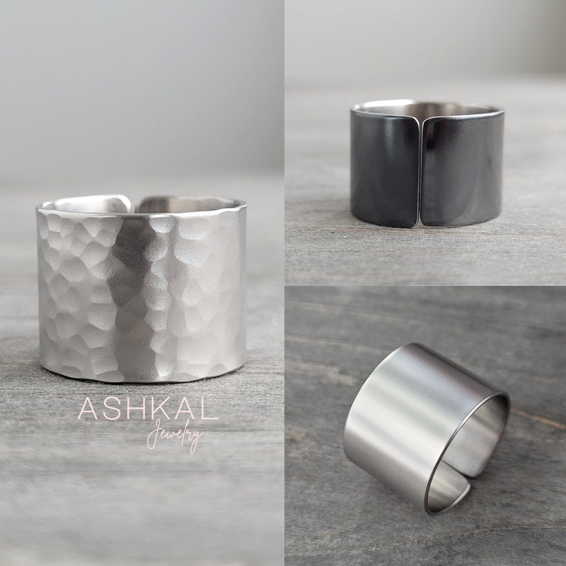 May include: Three silver rings, one with a hammered finish, one with a smooth finish, and one with a black oxidized finish. The rings are all wide and flat, and they are made of metal. The rings are on a gray wooden surface. ASHKAL Jewelry.