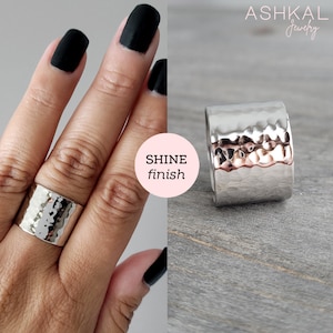 May include: A silver hammered wide band ring with a shiny finish. The ring is worn on a finger with black nail polish.
