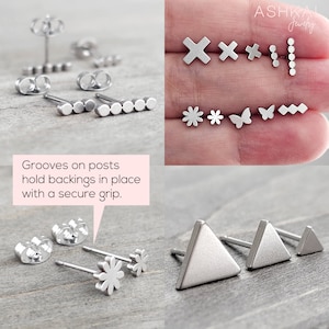 May include: A set of silver stud earrings with various geometric and floral designs. The earrings are displayed on a wooden surface and a hand. The text "Grooves on posts hold backings in place with a secure grip." is visible in the image.