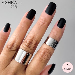 May include: Two silver rings, one wider than the other, worn on a hand with black nail polish. The rings are simple and modern in design. 2 RINGS.