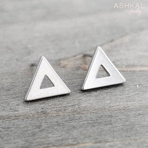 May include: A pair of silver triangle stud earrings with a hollow center. The earrings are on a wooden surface.