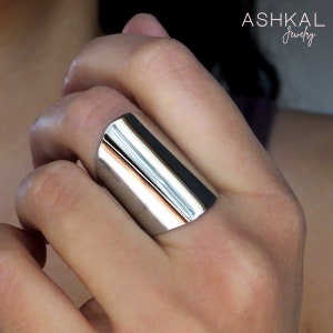 May include: A silver, wide, rectangular band ring. The ring is polished and shiny.