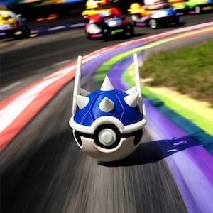 May include: A blue and white novelty item resembling a spiky turtle shell, positioned on a race track with colorful stripes. Miniature race cars blur in the background, suggesting speed and motion. The item is a playful, themed collectible.