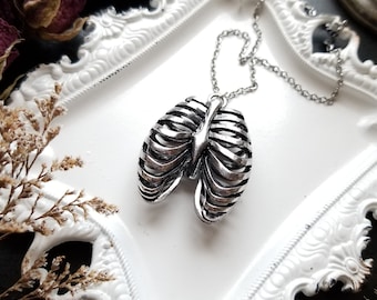 Puede incluir: Un collar de plata con un colgante de caja torácica. El colgante es detallado y realista, con una cadena de plata.