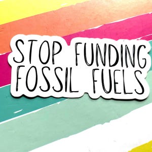 Puede incluir: Una pegatina blanca con el texto "STOP FUNDING FOSSIL FUELS" en negro, con una fuente de estilo manuscrito. La pegatina está colocada sobre un fondo de rayas diagonales de colores en amarillo, naranja, rosa, turquesa y blanco.