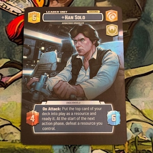 Puede incluir: Una tarjeta coleccionable con Han Solo de Star Wars. La tarjeta muestra un retrato de Han Solo en una cabina. La tarjeta incluye estadísticas del juego y texto, con una combinación de colores azul y negro. Unidad de líder.