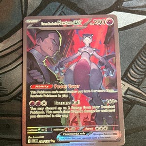 May include: A holographic Team Rocket's Mewtwo EX Pokémon card. The card features a purple Mewtwo and a man in a suit. The card text includes "Power Saver" and "Erasure Ball" abilities, with a HP of 280.