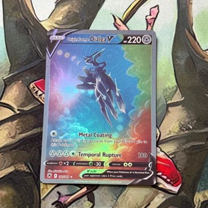 Pode incluir: Um cartão Pokémon Dialga V Forma Origem holográfico. O cartão apresenta uma criatura metálica azul escura contra um fundo colorido e rodopiante. O texto inclui "Metal Coating" e "Temporal Rupture". O cartão tem 220 HP.