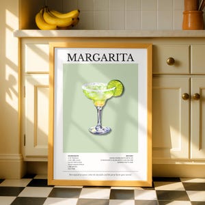 Op de afbeelding: Een ingelijste print met een margarita cocktail illustratie. Het kunstwerk toont een margarita glas met een limoenpartje, tegen een lichtgroene achtergrond. Het woord "MARGARITA" staat bovenaan, met de ingredi&euml;nten en methode eronder.