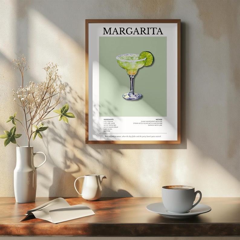 Op de afbeelding: Een ingelijste print met een illustratie van een margarita-cocktail. De drank zit in een glas met een zoutrand en limoengarnituur, tegen een lichtgroene achtergrond. Het woord "MARGARITA" staat bovenaan.