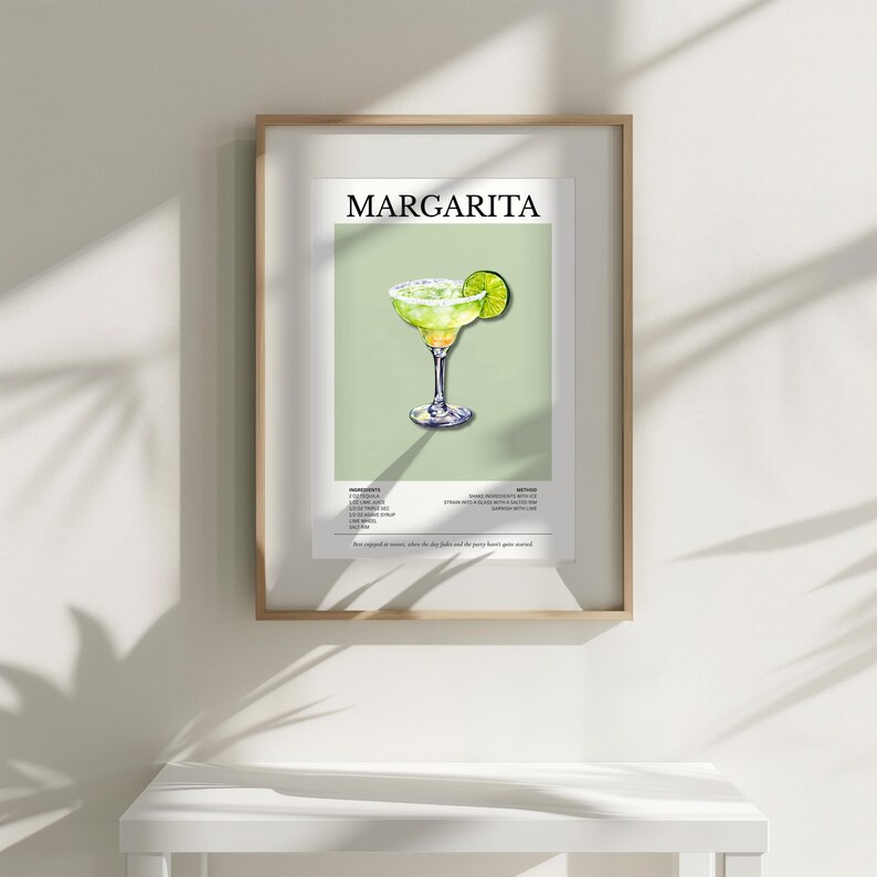 Op de afbeelding: Een ingelijste print met een margarita cocktail illustratie. Het kunstwerk toont een margarita in een glas met een limoenpartje, tegen een lichtgroene achtergrond. Het woord "MARGARITA" staat bovenaan.