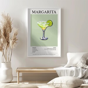 Op de afbeelding: Een ingelijste print met een margarita cocktail illustratie. Het kunstwerk toont een margarita in een glas met een steeltje met een limoenpartje, tegen een lichtgroene achtergrond. Het woord "MARGARITA" staat bovenaan.