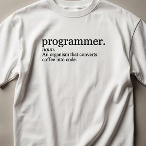 Op de afbeelding: Een wit T-shirt met korte mouwen en zwarte tekst op de borst die luidt: programmer. noun. An organism that converts coffee into code. Het shirt heeft een ronde hals en een standaard pasvorm, waarbij de gedrukte definitie duidelijk zichtbaar is.